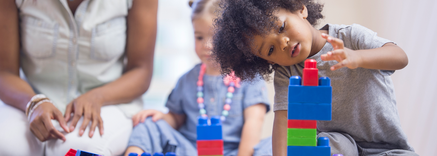 Young child playing with blocks with teacher in the background