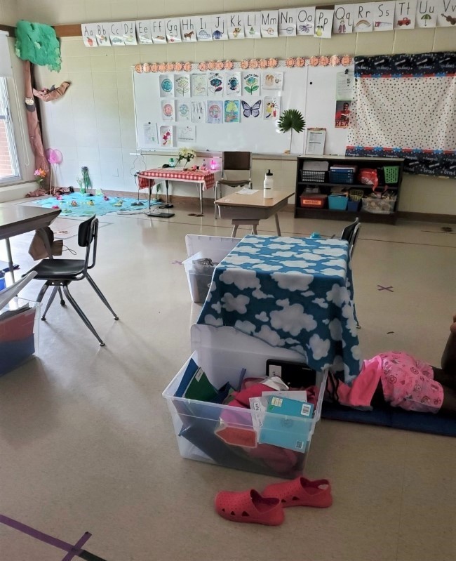 Classroom with a small table that has a blanket draped over it and a large bin filled with notebooks next to it